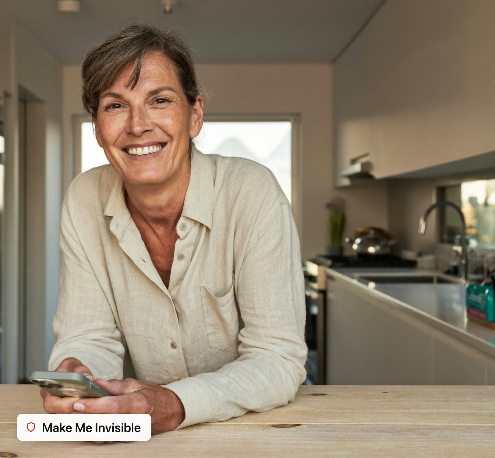 Woman in her fifties at her kitchen bench, phone in hand, smiling