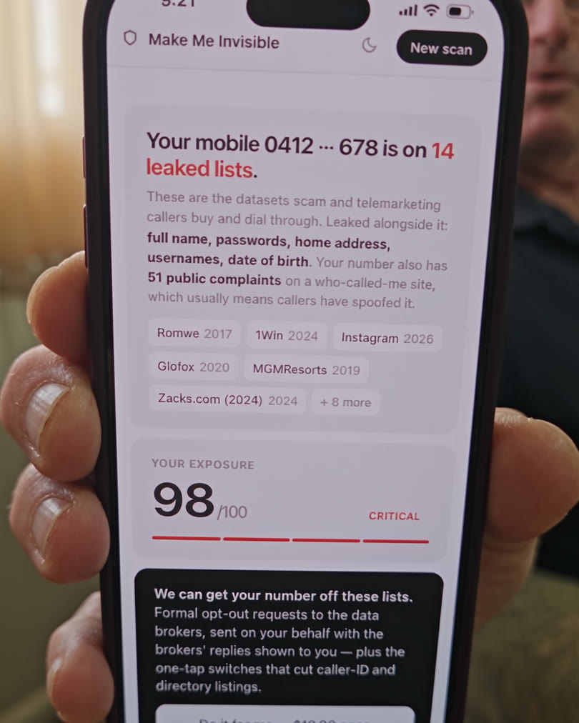 Man in a lounge room holding up a phone showing his Make Me Invisible result